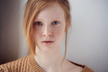 Portrait of beautiful pensive girl with red hair at home. Cute redhead and freckles woman face closeup portrait with healthy skin.