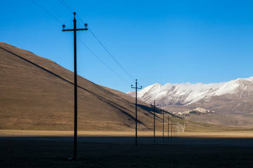 Electric pole line in Campo Imperatore plateau . Mountain with snow in background 