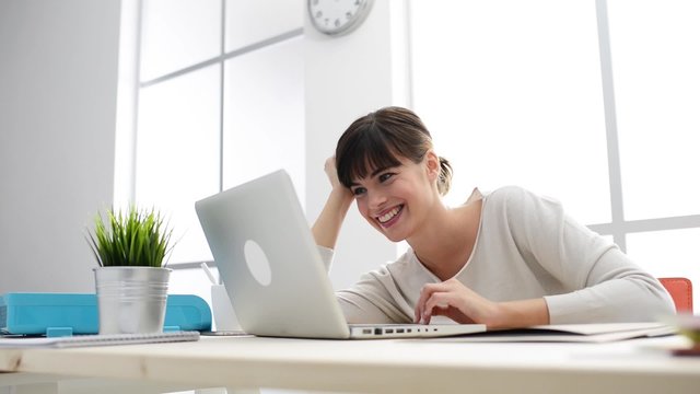 Smiling woman sitting at desk, social networking and connection with a laptop, communication and social networks concept