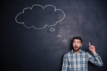 Inspired man pointing up and having an idea over blackboard