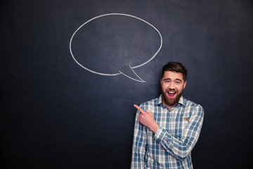 Cheerful man pointing away over blackboard background with  speech bubble