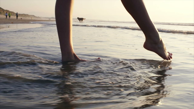 Low section of woman playing with water on shore. Side view of female with bare feet standing in water. She is touching water with toe at beach.