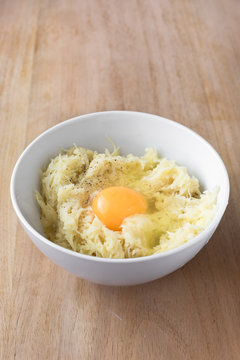 Raw grated potatoes and egg in white bowl