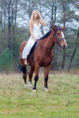 Fototapeta premium romantic sensual girl in white dress on a horse in the forest