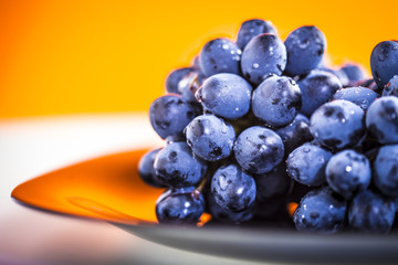Ripe bunch of  blue grapes on plate with shining water drops 