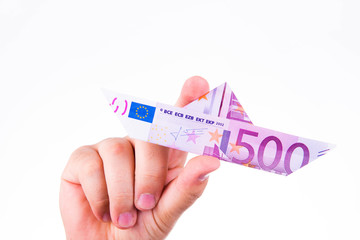 A hand holding a paper boat made with a 500 euro note on white background