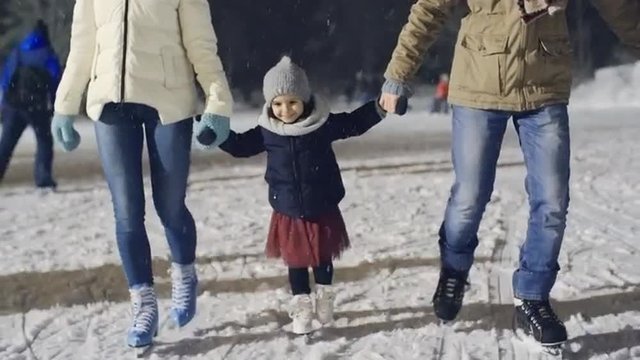 Adorable little girl enjoying ice skating with her parents at outdoor rink in park 