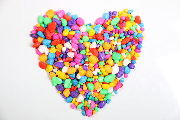 Colored stones arranged in a heart shape on white background.