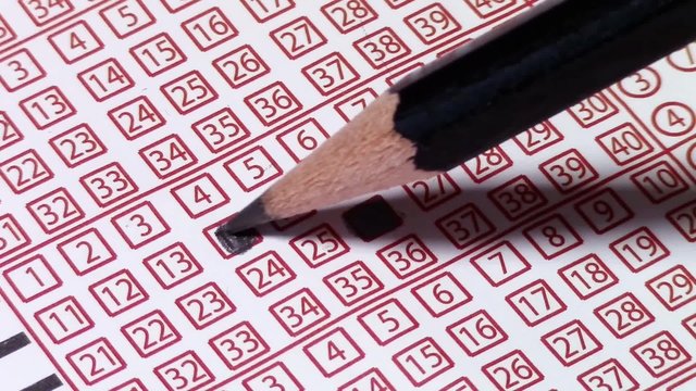 Marking with charcoal pencil several lucky numbers to be played , on a paper lottery ticket, close-up