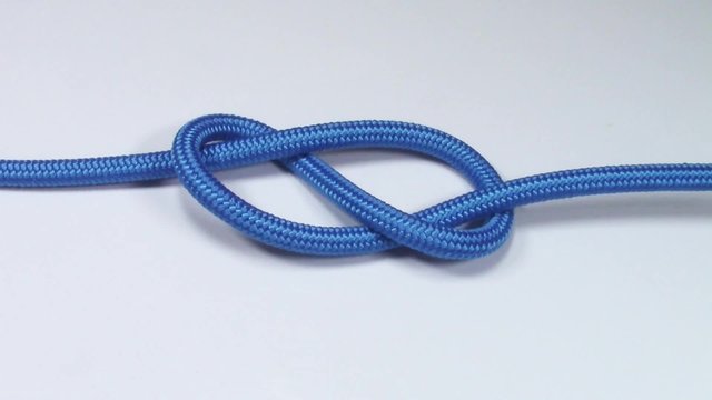 Figure eight knot made from blue synthetic rope, tightening on white background