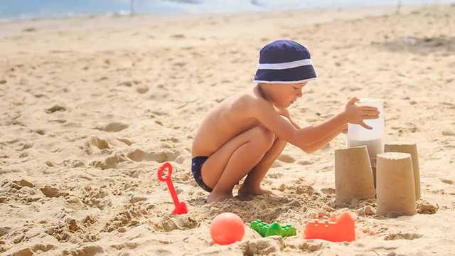 Little Boy in Hat Squats Removes Bucket to Make Sand Cake