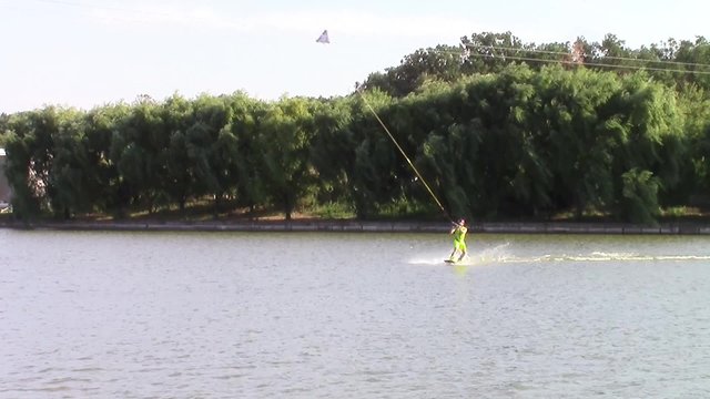 Water skier being pulled on the surface of a lake by a ski cable installation , performing a jump
