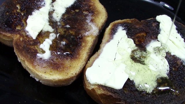 Couple of buttered toasted slices of bread with honey being poured on one of them, closeup