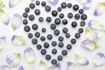 Blueberries heart with flower petals directly from above on white background 