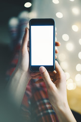 close-up of a smartphone with a blank screen in the hands of a girl in a homely atmosphere background bokeh light
