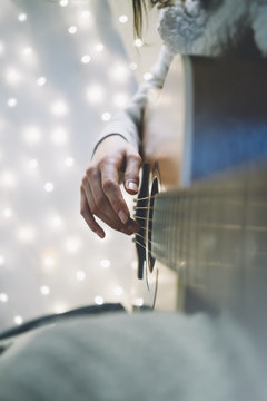 Closeup of a man playing the guitar in a homelike atmosphere, sitting in a chair against a background of bokeh light vertical