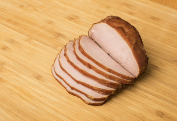Homemade Canadian bacon on cutting board with tomato, onion, bread rolls for sandwich preparation
