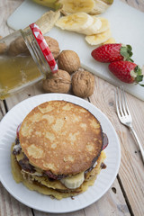 pancakes with banana, nuts and strawberry on wooden background