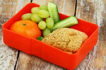 Healthy lunch box containing mixed grain cheese roll, mandarine, grapes and cucumbers sticks
