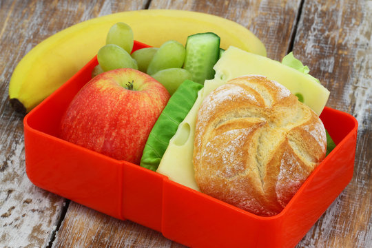 Lunch box containing cheese sandwich with lettuce, apple, grapes and banana
