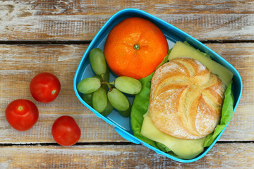 Lunch box containing cheese sandwich, grapes, mandarine and cherry tomatoes
