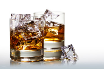 Two glasses of scotch whiskey with ice cubes, on white