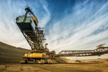 Fototapeta na wymiar One side of huge coal mining drill machine photographed from a ground with wide angle lens. Dramatic and colorful sky in background.