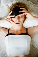 Portrait of a beautiful young blonde girl lying on a bed wearing a mask to sleep