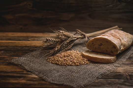 a ciabatta bread with wheat on stackcloth on a wooden rustic background