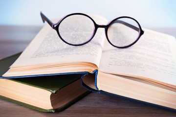 Books and eyeglasses on wooden table, close up
