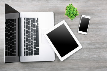 Modern laptop, smart phone and tablet with small green plant on a wooden table