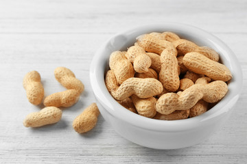 Peanuts in the bowl on white wooden background