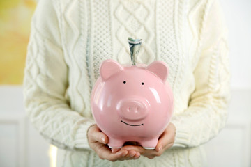 Woman holding piggy bank with inserted dollar banknote. Savings money concept