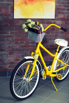 Yellow bicycle with books on brick wall background