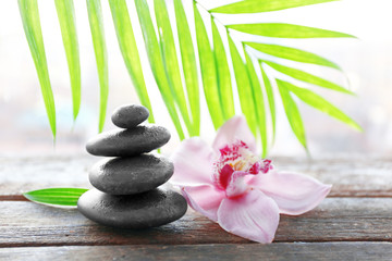 Fototapeta na wymiar Spa stones with palm leaves and pink orchid on wooden background