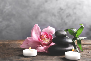 Spa stones with bamboo, pink orchid and candles on wooden table against grey background