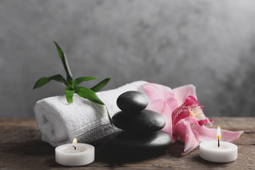 Spa stones with pink orchid, candles, bamboo and towel on wooden table against grey background
