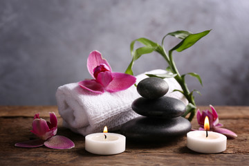 Obraz na płótnie Canvas Spa stones with candles, purple orchid, bamboo and towel on wooden table against grey background
