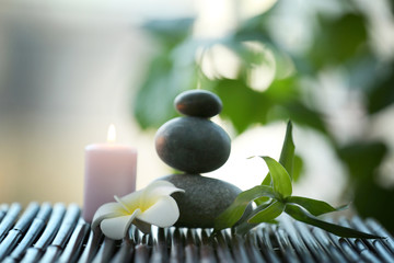 Spa stones with candle and tropical flower on blurred background