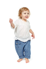 Child 24 months, 2 years, smiles, raises his right hand, as a bud is dancing on a white background isolation stands in jeans and a white shirt.