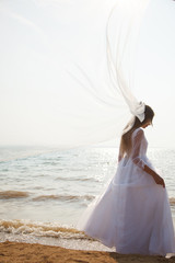Fototapeta na wymiar Bride is standing on the beach with Long flying veil