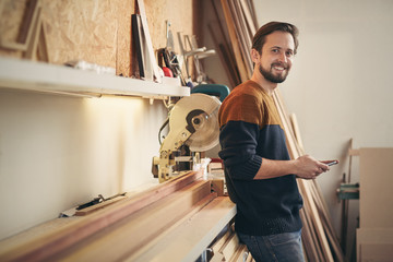 Young carpenter looking up while using phone in his workshop
