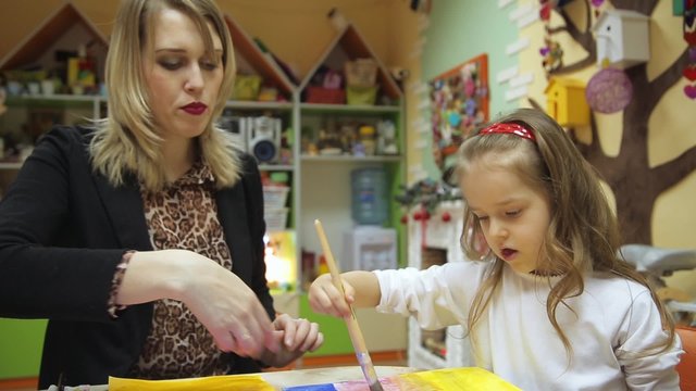 The teacher helps the little girl to paint