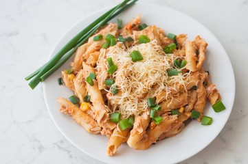 Penne pasta with healthy tuna fish, cheese and chopped scallion or spring onion leaves. Served on a white oval plate