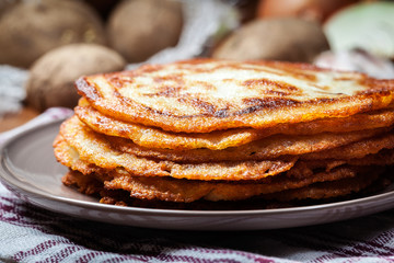 Stack of potato pancakes on a wooden table. In the background potatoes