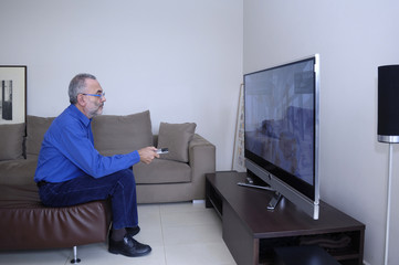  Mature Man Watching Television And Using Remote Control