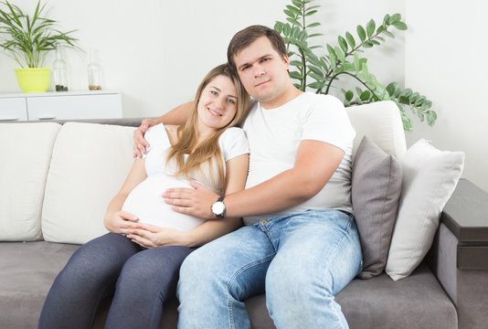 Happy couple waiting for baby posing on sofa at living room