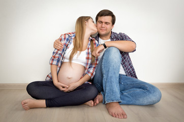 portrait of happy pregnant couple sitting on floor and leaning o