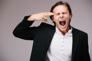 Tired young man in shirt and tie gesturing handgun near his head and looking at camera. Business suicide.