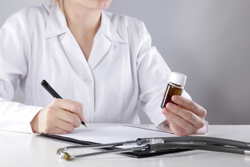 Fototapeta premium Young woman physician with stethoscope prescribing treatment to patient. Female doctor writing recipe on clipboard in hospital.